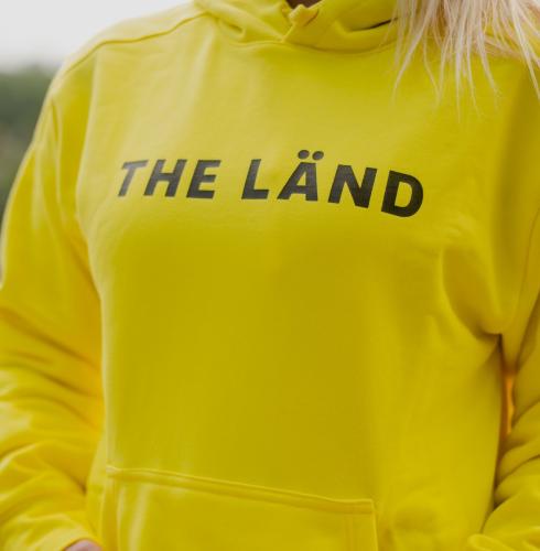 Gelber Kapuzenpullover mit der Aufschrift THE LÄND
